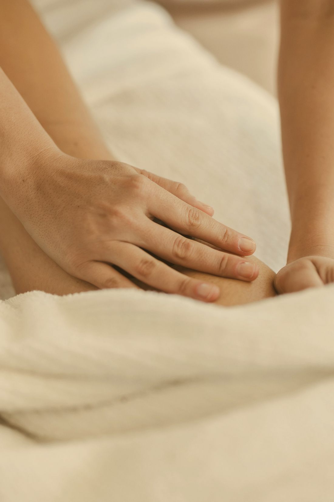 Mains posées avec douceur sur une jambe, linge blanc